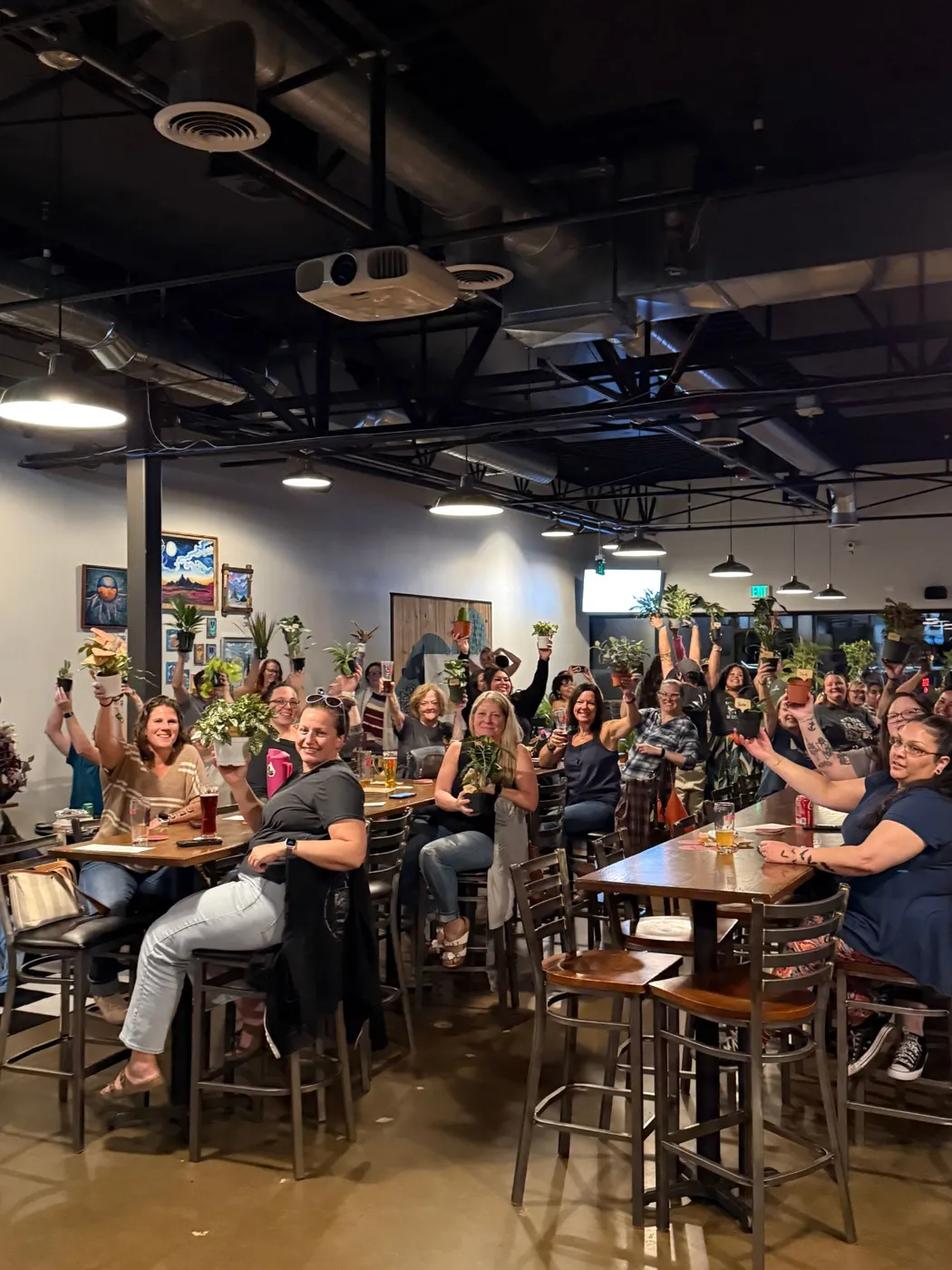 A packed brewery of smiling players holding potted plants over their heads