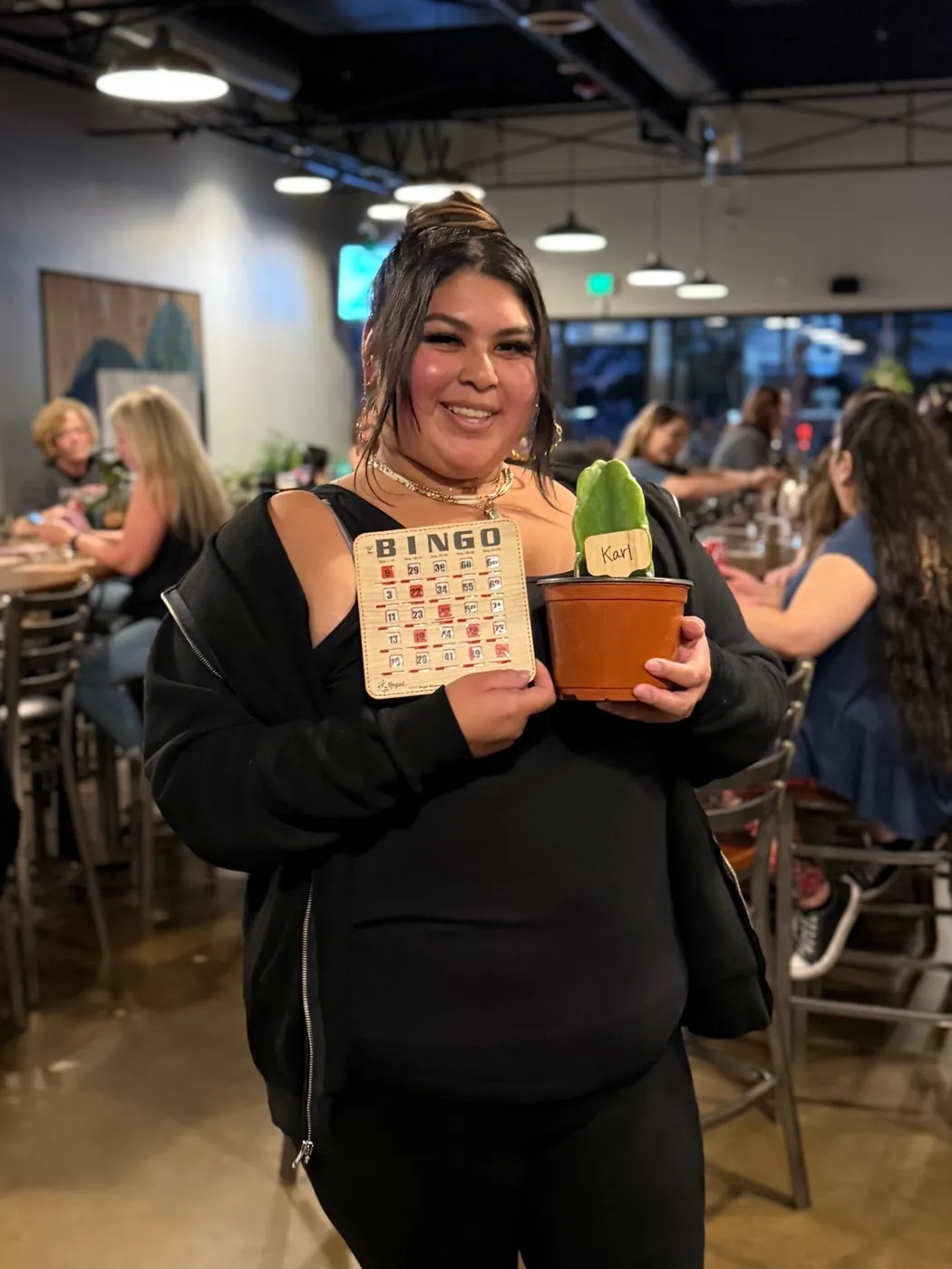 A smiling woman holding a bingo card and a small cactus in a terracotta pot