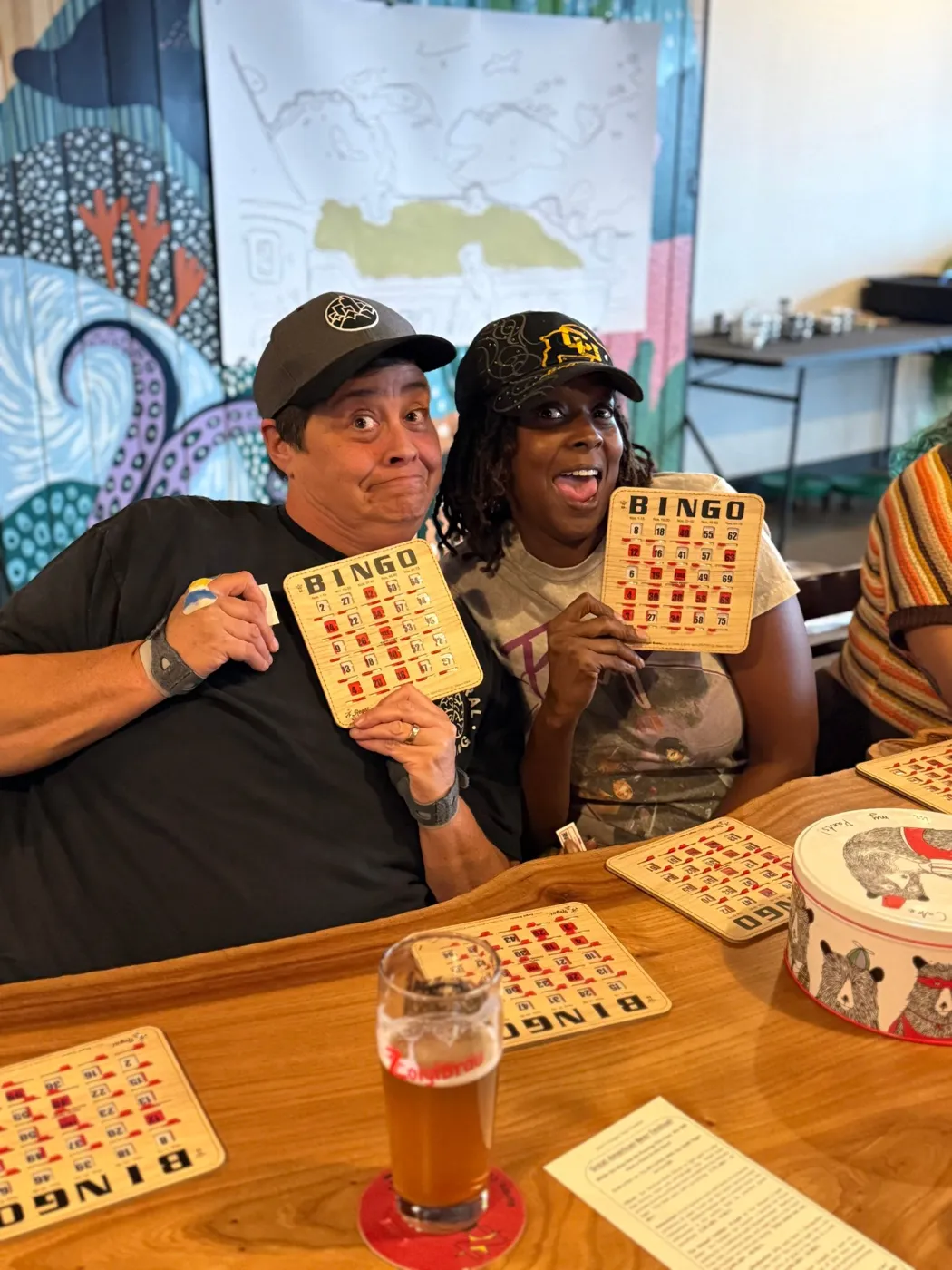 Two friends in baseball caps making silly faces and holding up wooden bingo cards